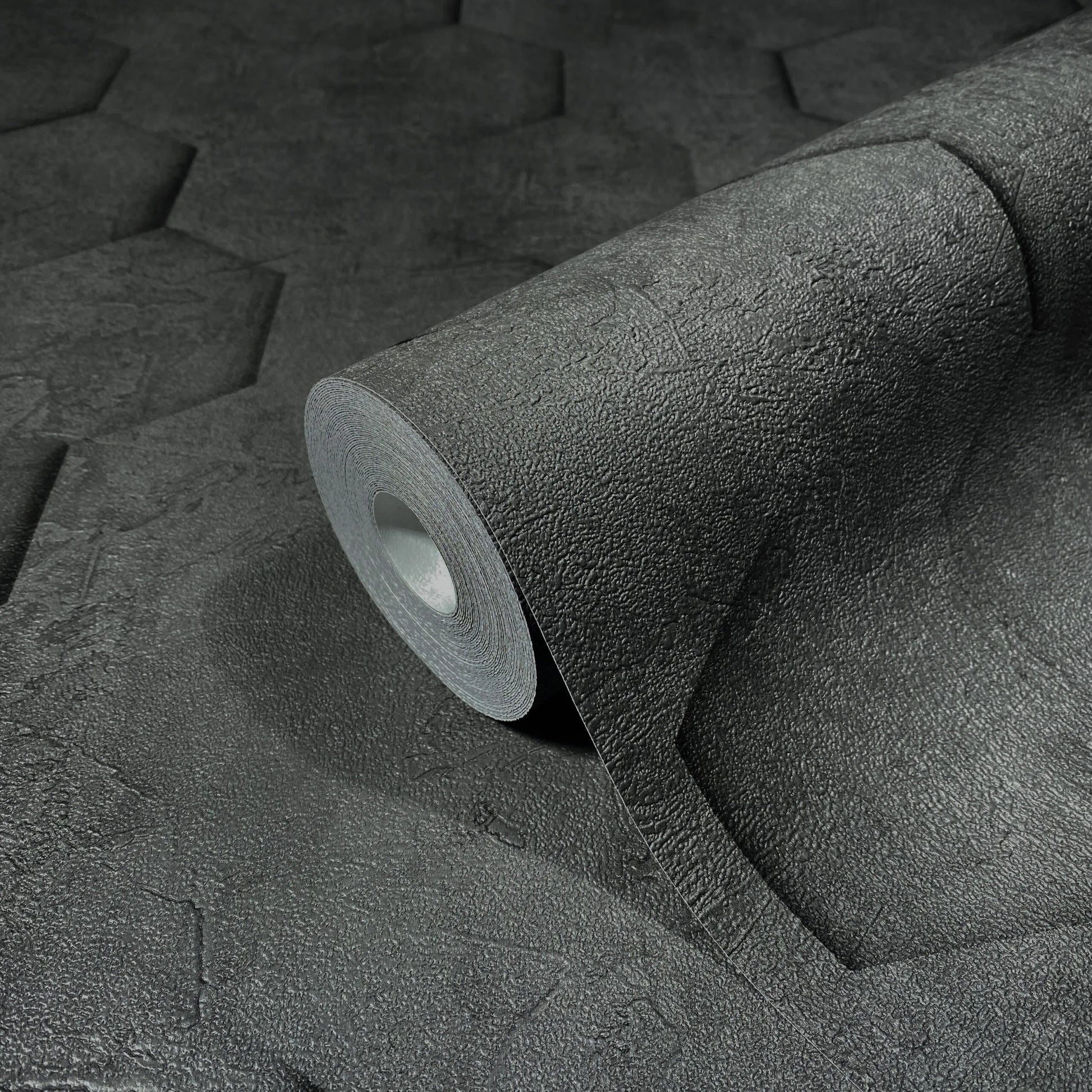 Marburg Loft Superior 34161 Close-up of a dark charcoal wallpaper roll on matching material, showing a rough texture with large embossed hexagon shapes.