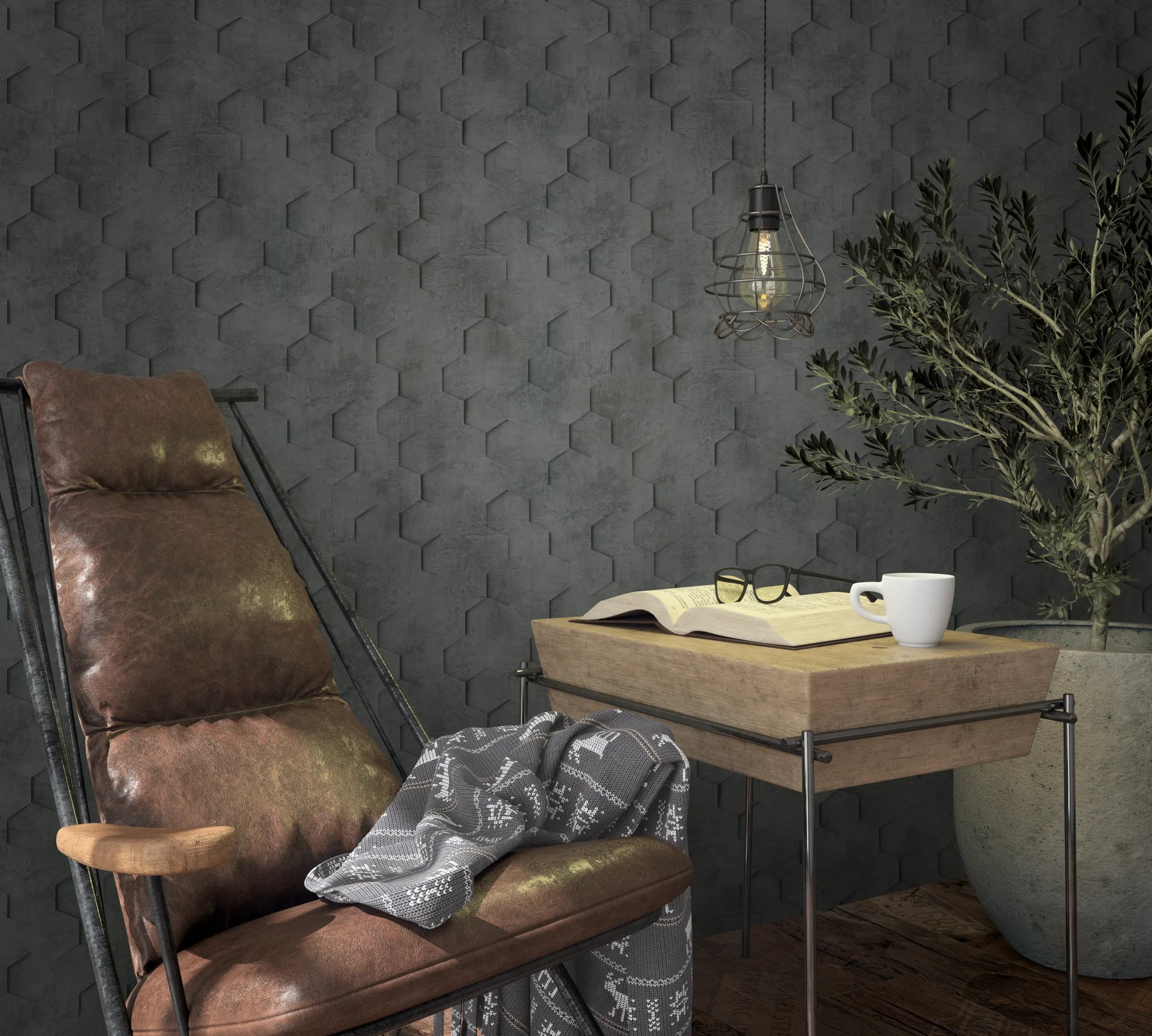 Marburg Loft Superior 34161 Dark charcoal wallpaper with a geometric hexagon pattern creating a subtle 3D effect. Shown with a leather lounge chair, a small wooden table holding an open book, glasses and a mug, a wire-cage pendant light, and a large potted plant.