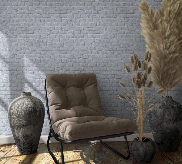 Marburg Loft Superior 34167 Gray brick wallpaper behind a cushioned lounge chair, ceramic vases, and dried pampas grass on a wooden floor.