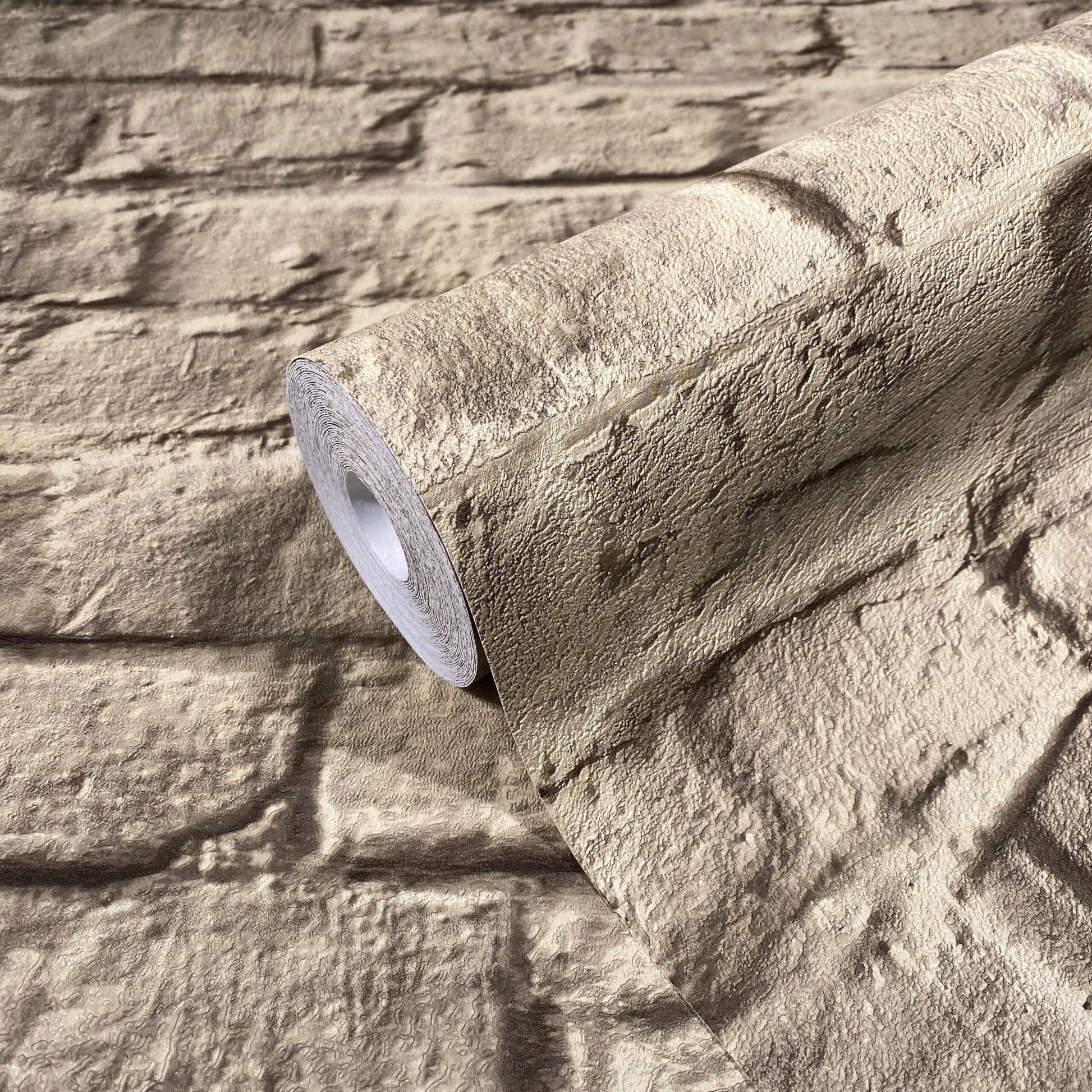 Marburg Loft Superior 34169 A roll of textured light brown wallpaper with irregular horizontal ridges resting on a matching unrolled sheet.
