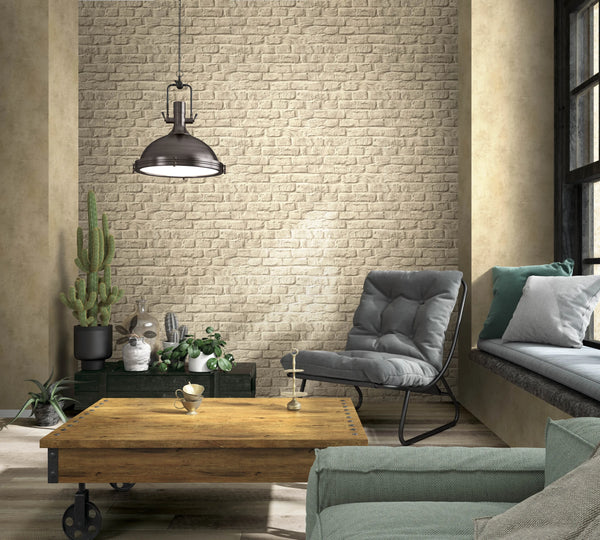 Marburg Loft Superior 34169 Beige faux brick wallpaper in a living room with a metal pendant light, gray lounge chair, wooden coffee table on casters, window seat with cushions, and several potted plants.