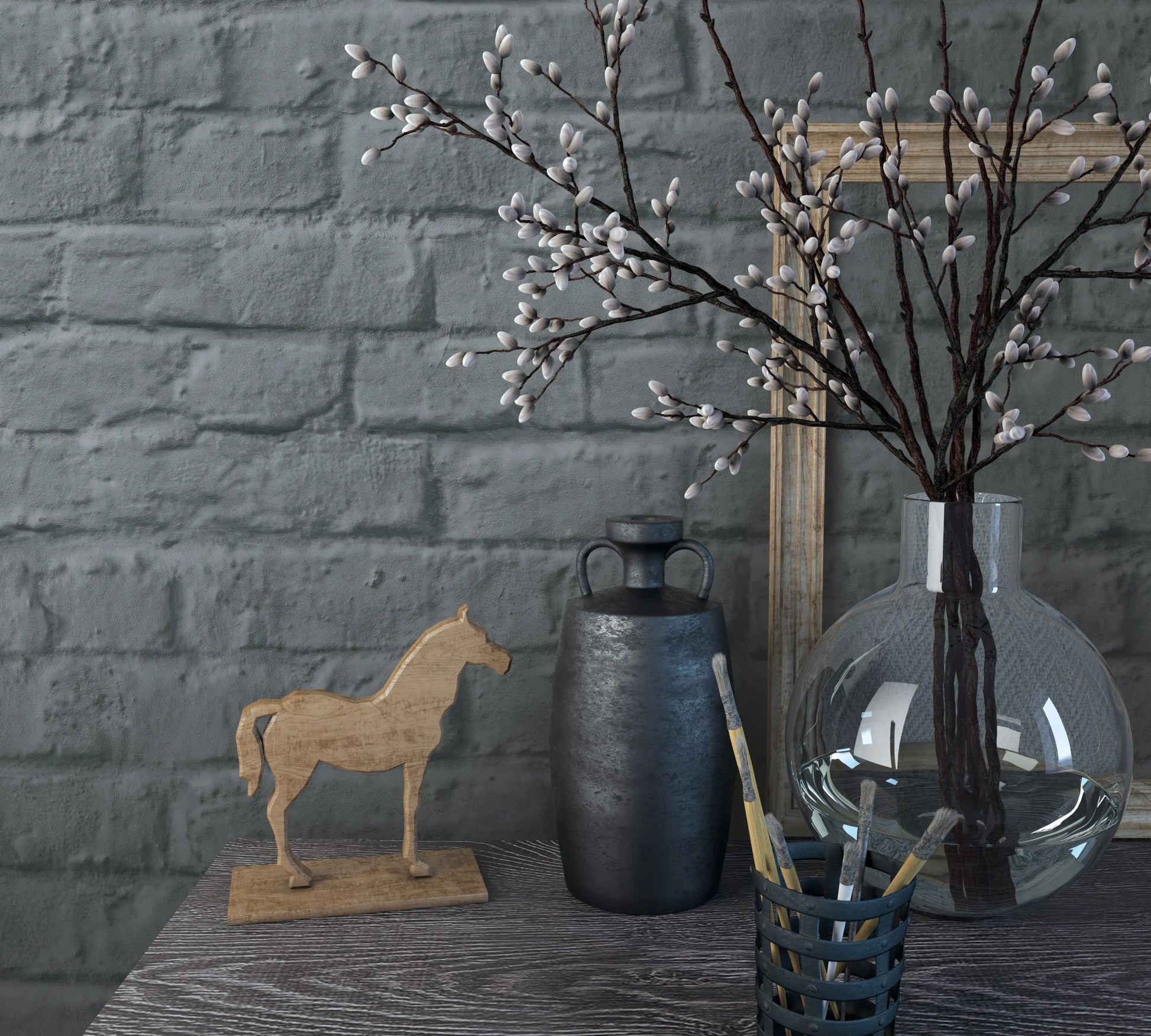Marburg Loft Superior 34170 Dark grey faux brick wallpaper behind a tabletop vignette with a clear glass vase holding budding branches, a dark jug, a wooden horse figurine, a cup of paintbrushes, and an empty wooden frame.