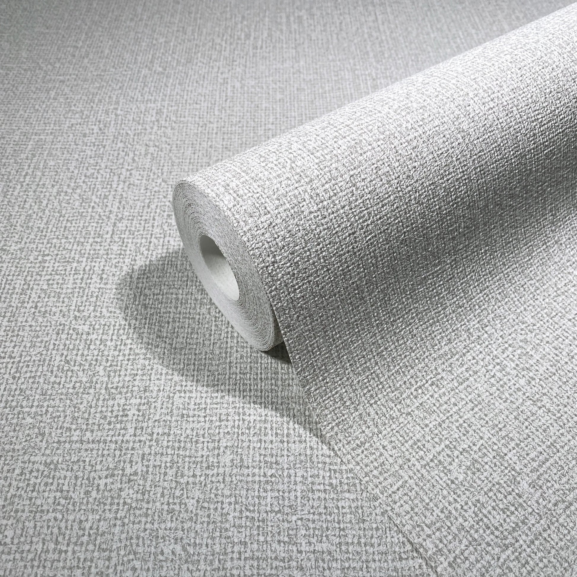 Marburg Loft Superior 34172 Angled wallpaper roll resting on matching light neutral crosshatch-textured wallpaper, highlighting the material and pattern.
