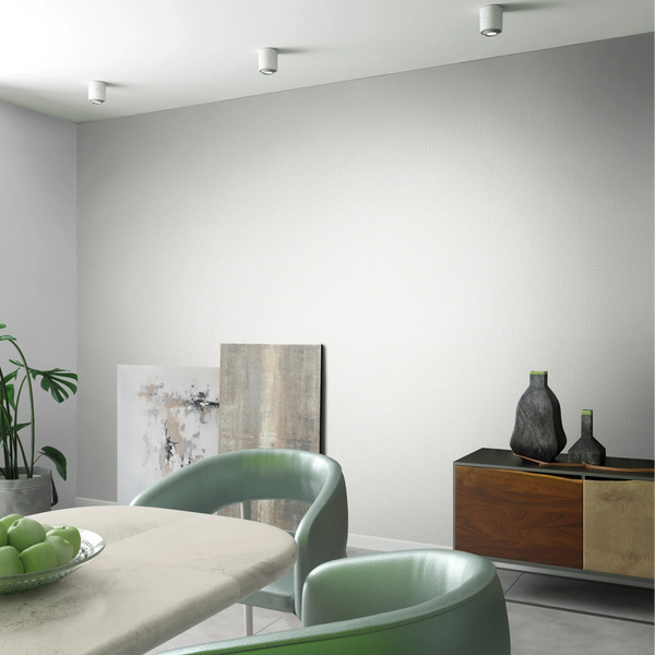 Marburg Loft Superior 34172 Light beige textured wallpaper on a dining room wall, shown with a marble-look table, green chairs, a bowl of green apples, a sideboard with decorative vases, a potted plant, and artwork resting on the floor.