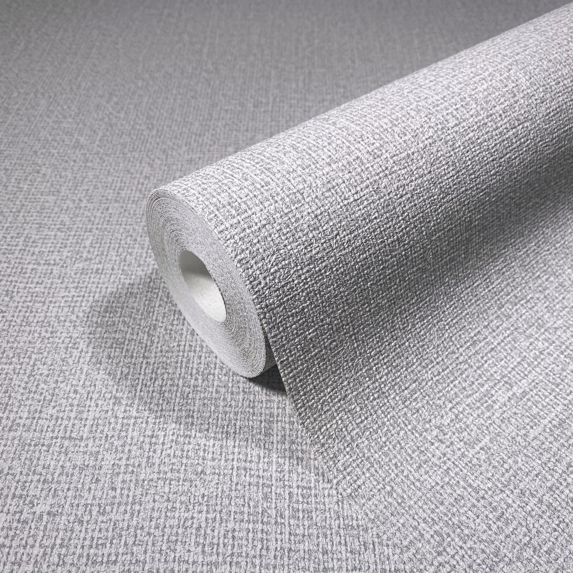 Marburg Loft Superior 34173 A gray wallpaper roll with a subtle crosshatch texture, shown partially unrolled on the same patterned surface.