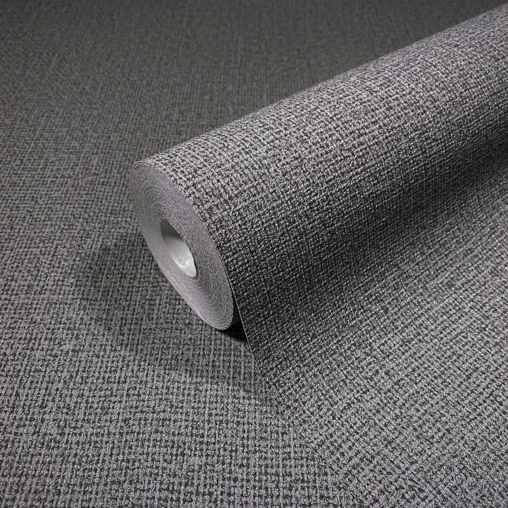 Marburg Loft Superior 34174 Angled roll of gray textured wallpaper with a small crosshatch grid, shown on a matching unrolled surface.