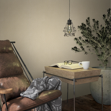 Marburg Loft Superior 34175 Beige textured wallpaper with a subtle woven pattern shown behind a leather lounge chair, a hanging cage pendant light, a wooden side table with an open book, glasses and a white mug, and a large potted plant.