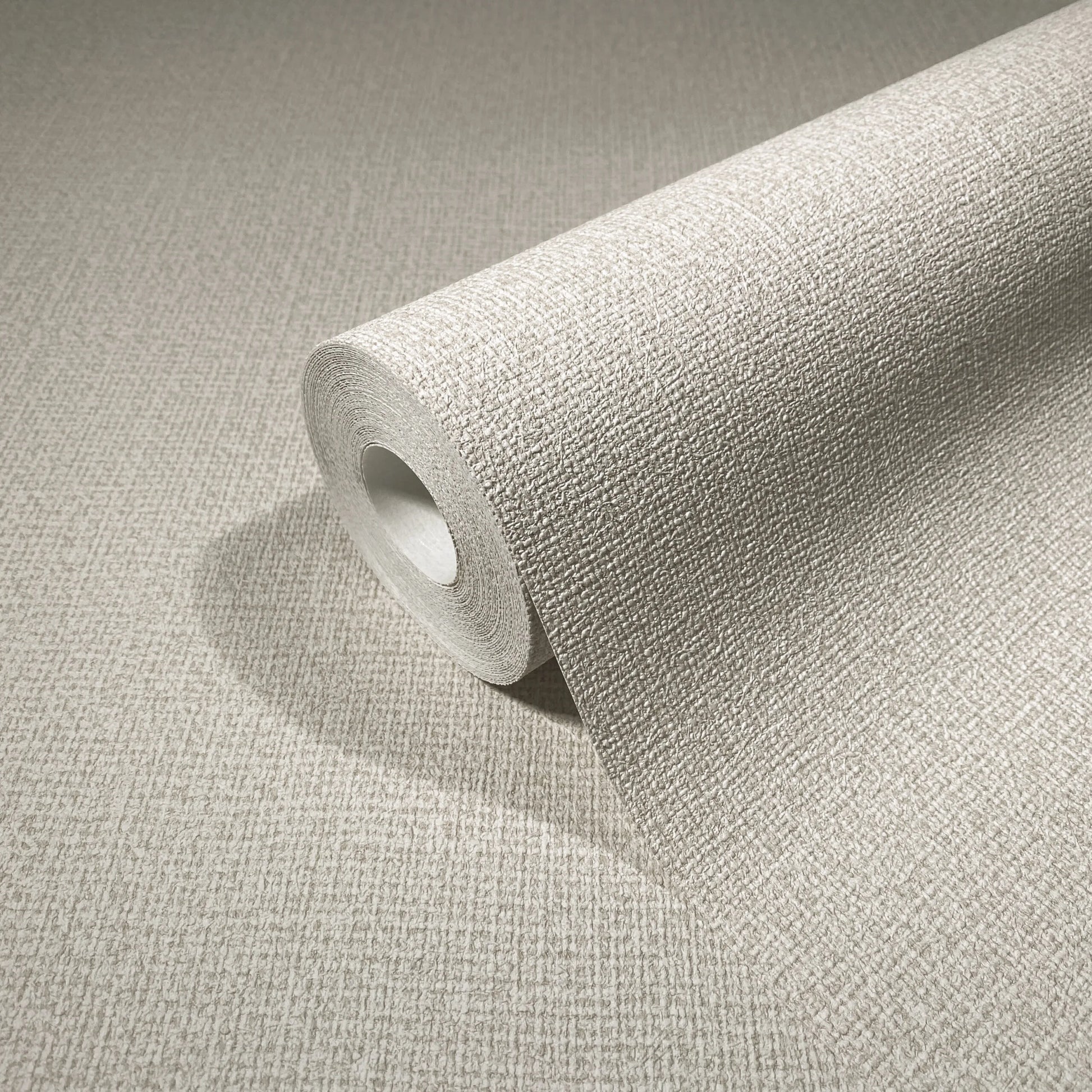 Marburg Loft Superior 34177 Close-up of a beige textured wallpaper roll on a matching surface, showing a fine crosshatch texture.