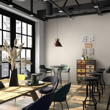 Marburg Loft Superior 34177 Industrial-style cafe interior showing a beige textured wallpaper feature wall, a hanging pendant light, bar stools at a counter, mixed chairs and tables, a colorful drawer cabinet with small wall art, and large black-framed windows.