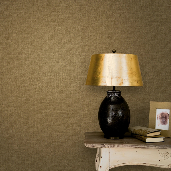 Marburg Loft Superior 34178 Brown textured wallpaper behind a black table lamp with a gold shade on a distressed console table, with books and a small framed photo.