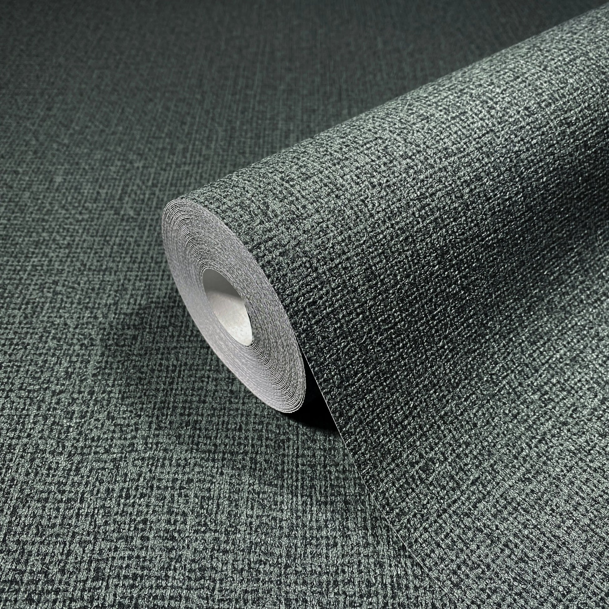 Marburg Loft Superior 34180 Close-up of a dark green textured wallpaper roll resting on matching unrolled wallpaper, showing a fine crosshatch pattern.