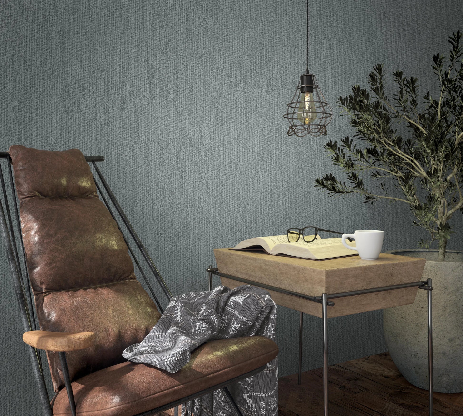 Marburg Loft Superior 34181 Muted green textured wallpaper behind a brown lounge chair, a wood side table with an open book, eyeglasses, and a white mug, a wire‑cage pendant light, and a large potted plant on a wood floor.