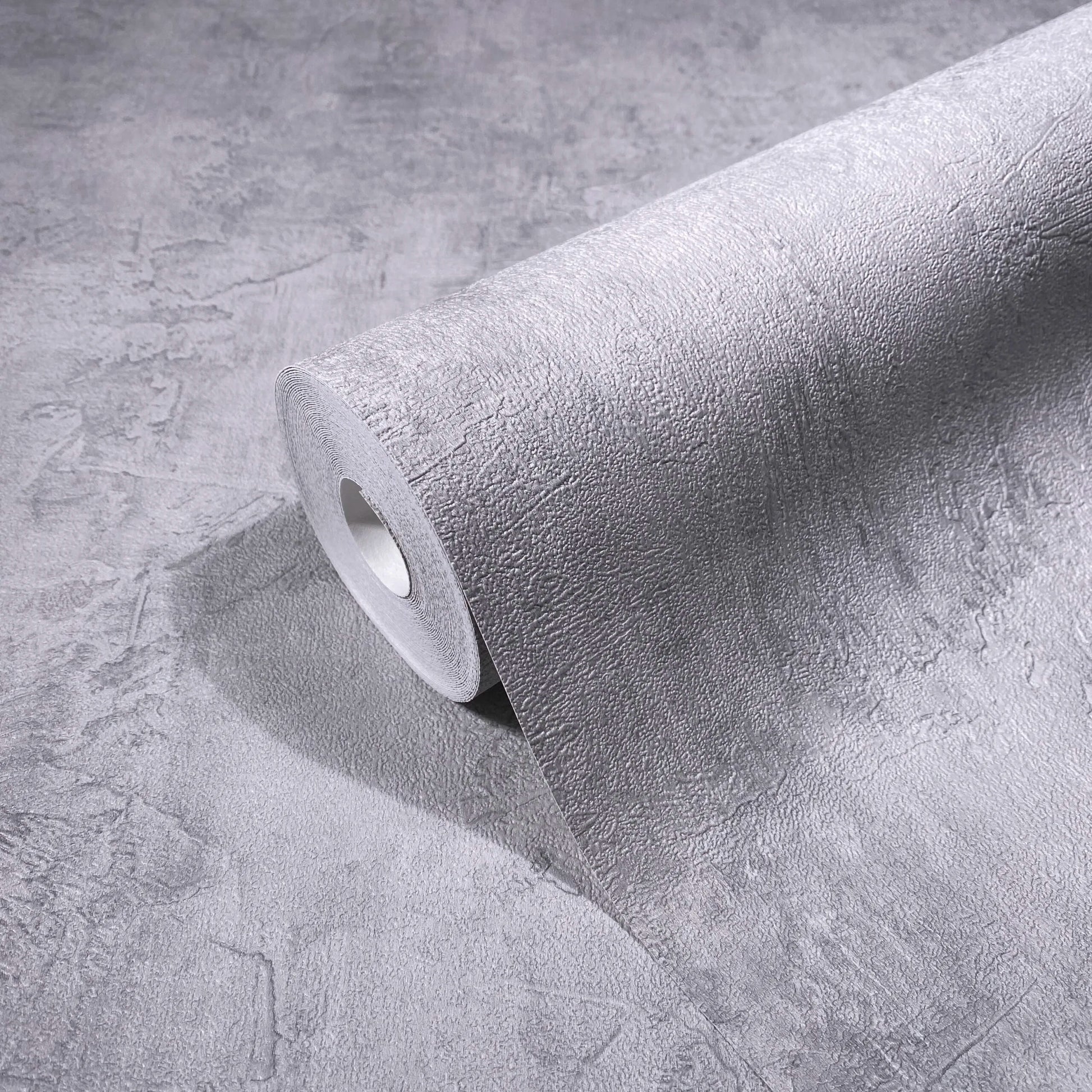 Marburg Loft Superior 34187 Gray textured plaster-effect wallpaper roll resting on a matching unrolled sheet, showing the irregular stucco pattern.