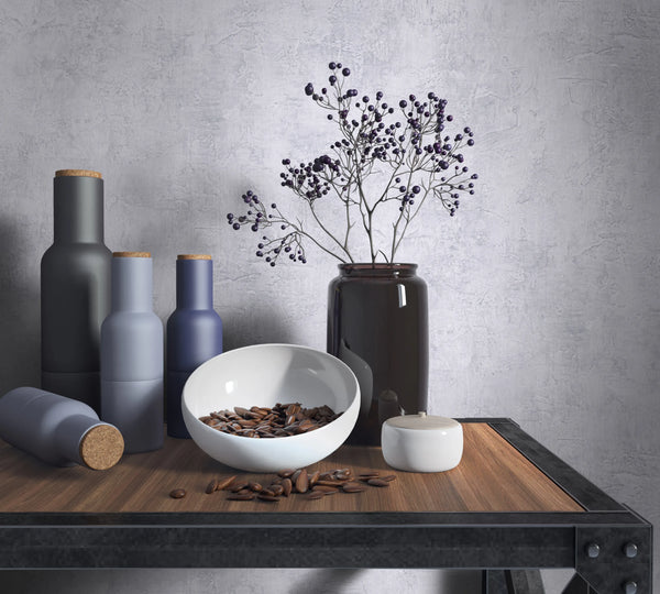 Marburg Loft Superior 34187 Gray textured wallpaper with a plaster effect behind a wood and metal shelf styled with matte bottles, a dark glass vase holding berry branches, a white bowl with brown seeds, and a small lidded jar.