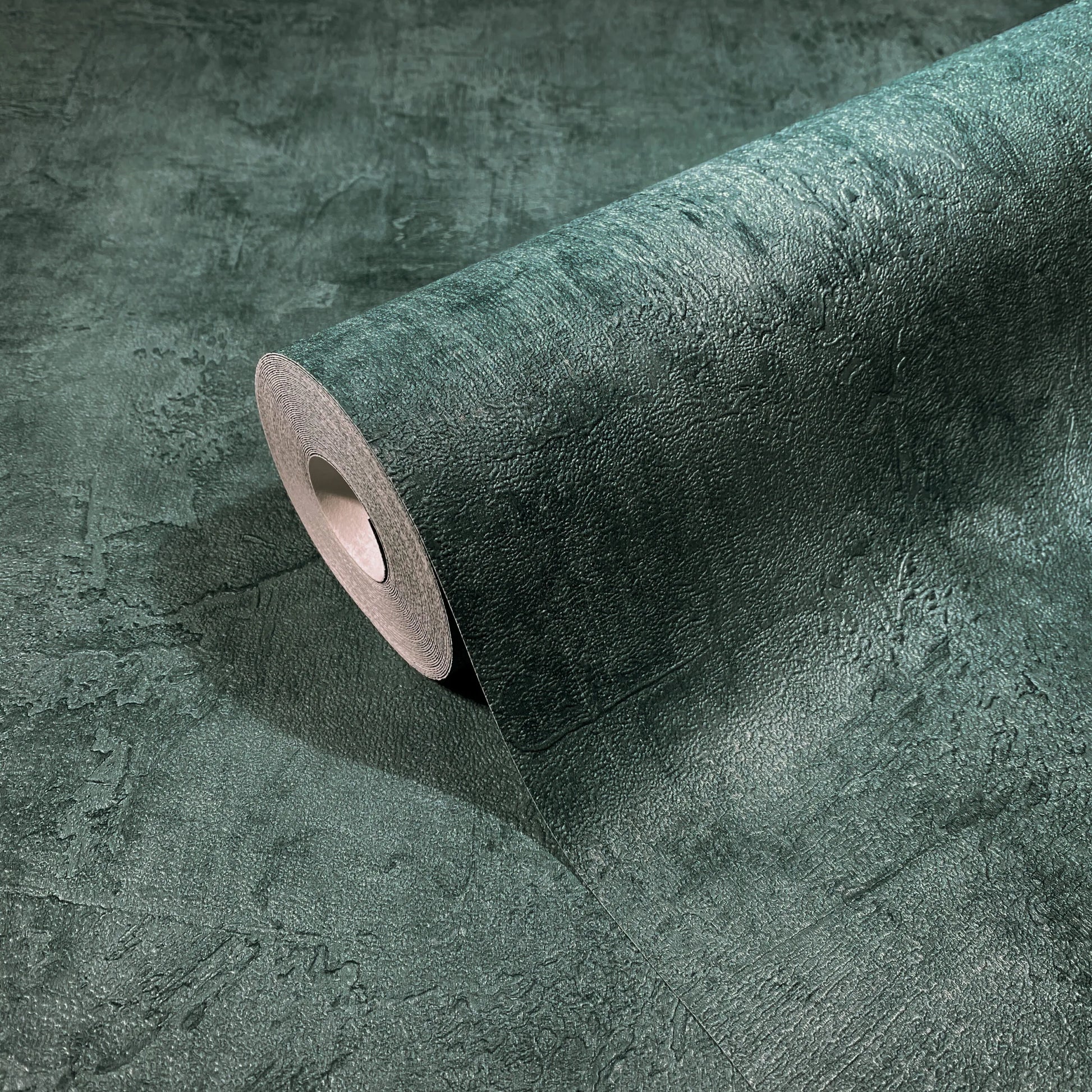 Marburg Loft Superior 34189 A roll of dark green textured wallpaper partially unrolled on a matching surface, showing a mottled, plaster-like pattern.