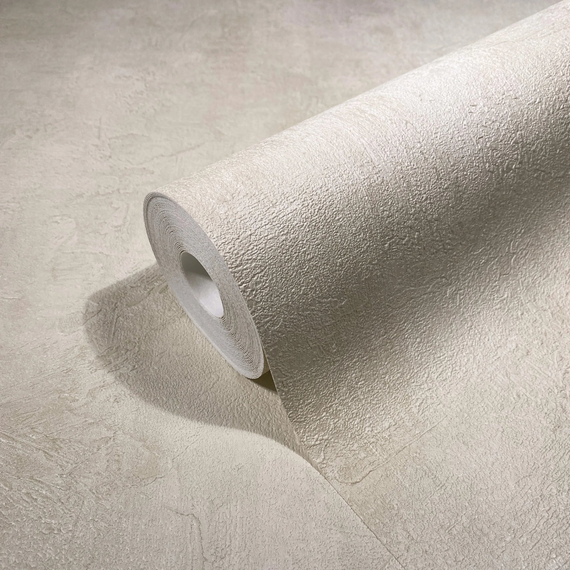 Marburg Loft Superior 34191 A light beige wallpaper roll with a subtle plaster-like texture unrolling across a matching surface.