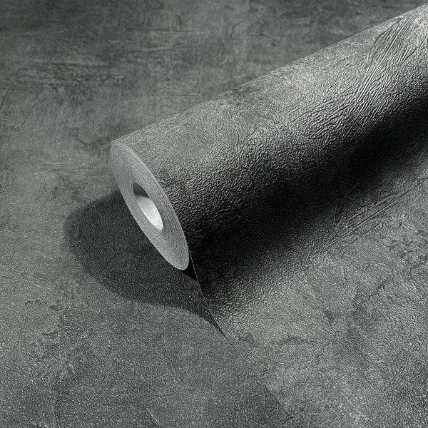 Marburg Loft Superior 34193 A dark anthracite wallpaper roll partially unrolled, displaying a textured, plaster-like surface.