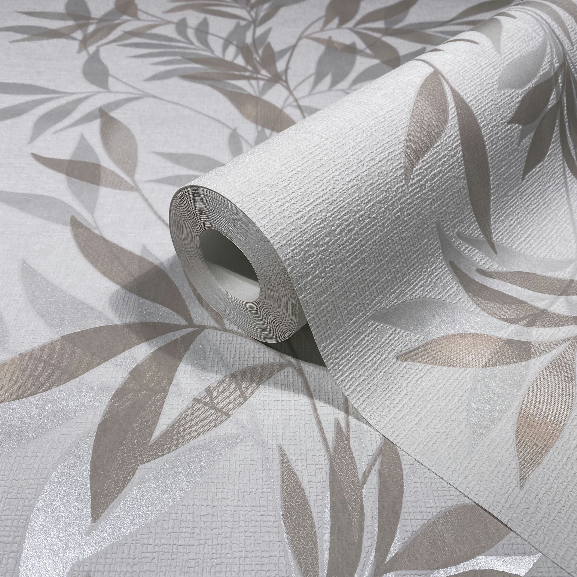 Marburg Mona 82459 Close-up of a wallpaper roll on matching unrolled wallpaper, showing a textured white background with a beige leaf pattern.