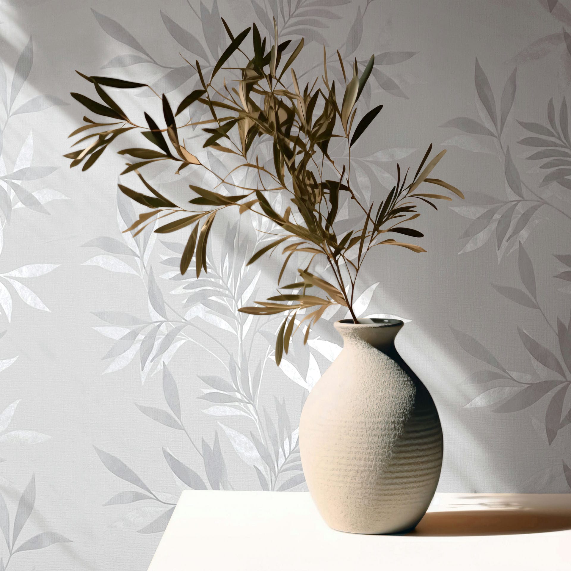 Marburg Mona 82460 Gray and white leafy wallpaper with a subtle sheen, styled with a textured ceramic vase holding a branch on a light surface, sunlight casting shadows.