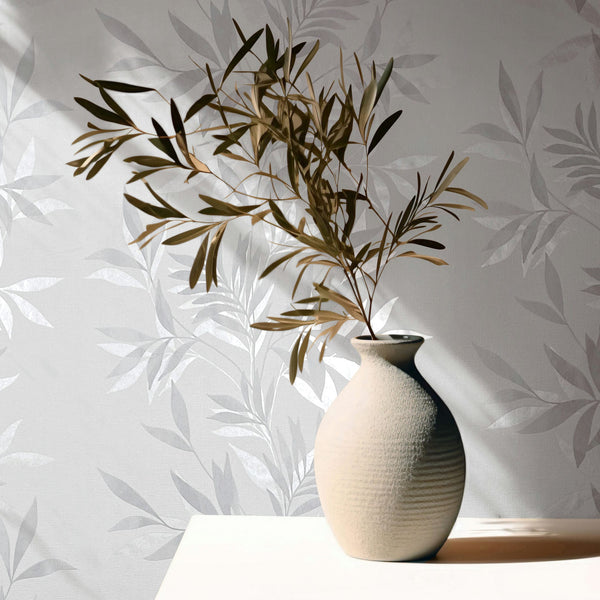 Marburg Mona 82460 Gray and white leafy wallpaper with a subtle sheen, styled with a textured ceramic vase holding a branch on a light surface, sunlight casting shadows.