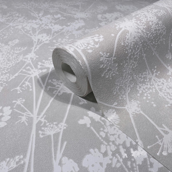 Marburg Mona 82464 A wallpaper roll partially unrolled on a matching surface, showing a light gray textured ground with glossy white botanical silhouettes.