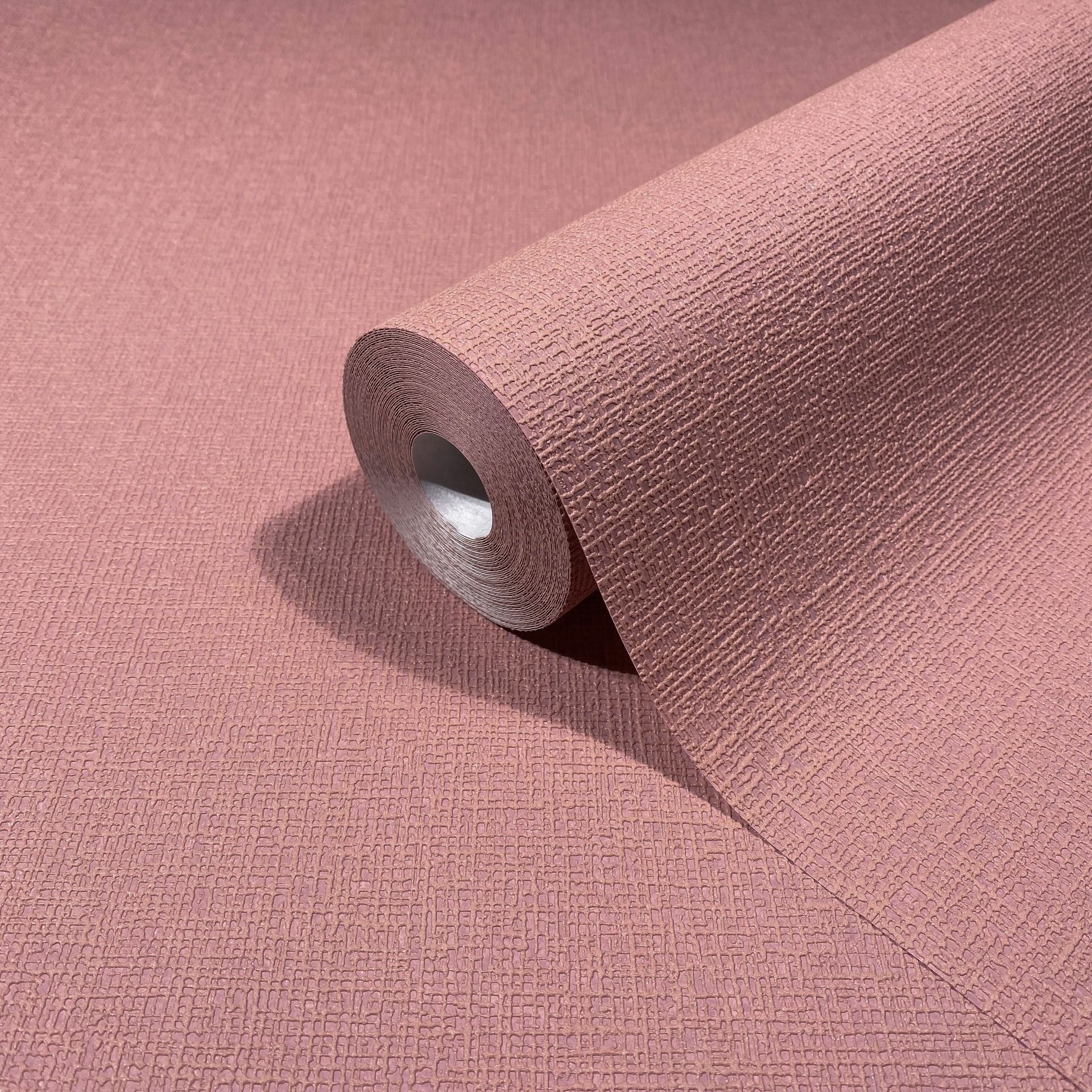 Marburg Mona 82467 A warm rose-red wallpaper roll with a fine embossed block texture, shown partially unrolled on the same material.