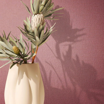 Marburg Mona 82467 Close-up of a red textured wallpaper with fine vertical lines, styled with a cream vase holding leafy flower stems and their shadows on the wall.