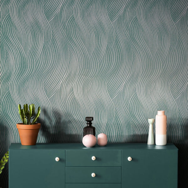 Marburg Mona 82478 Green wallpaper with flowing silver wavy line pattern behind a teal cabinet topped with a potted cactus and assorted vases.