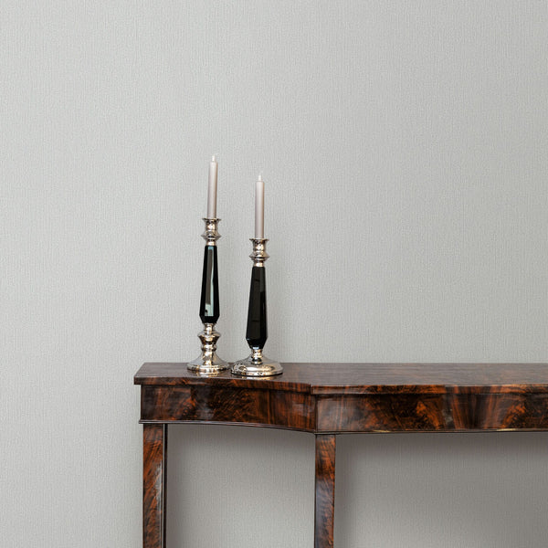 Marburg Mona 82479 Light gray textured wallpaper with a subtle vertical strie, shown behind a wooden console table with two tall candlesticks and tapers.
