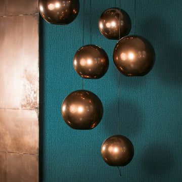 Marburg Mona 82482 Teal-green textured wallpaper with fine vertical broken lines, shown behind a cluster of bronze globe pendant lights; a metal panel is visible on the left edge.