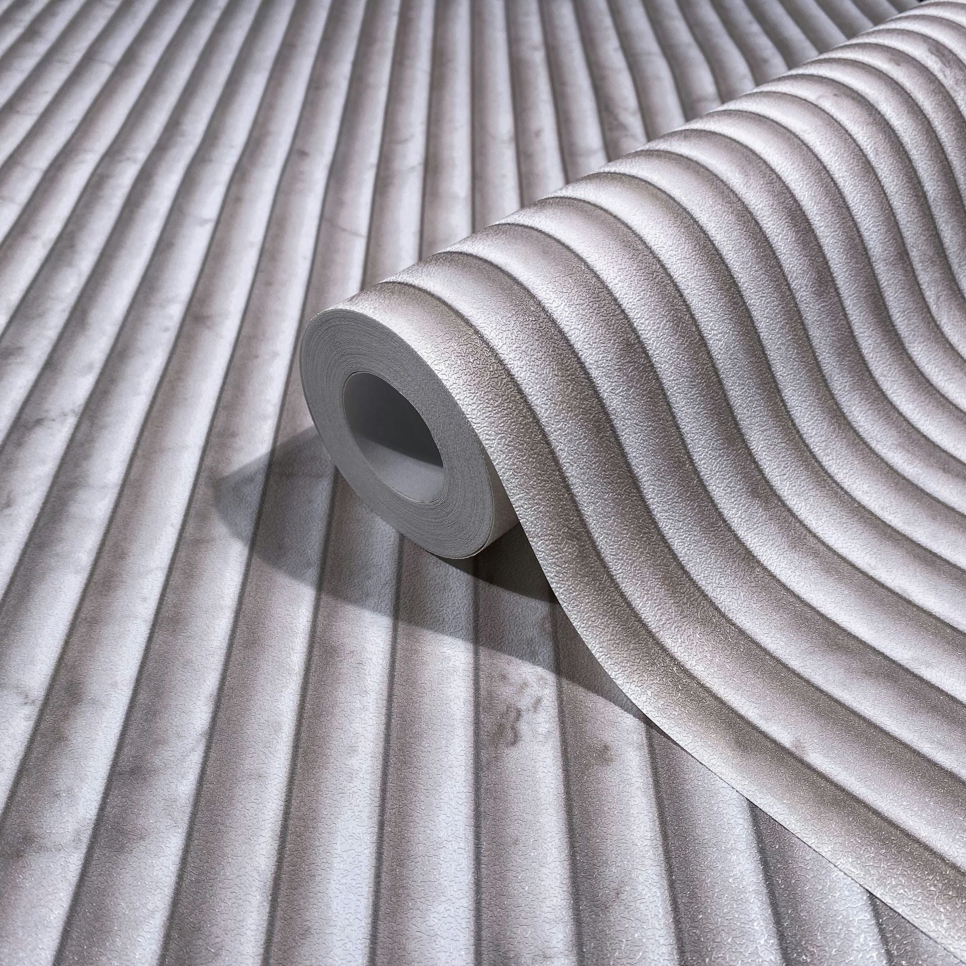 Marburg Mona 89004 Wallpaper roll on matching surface showing textured wavy ribbed stripes in beige and gray.