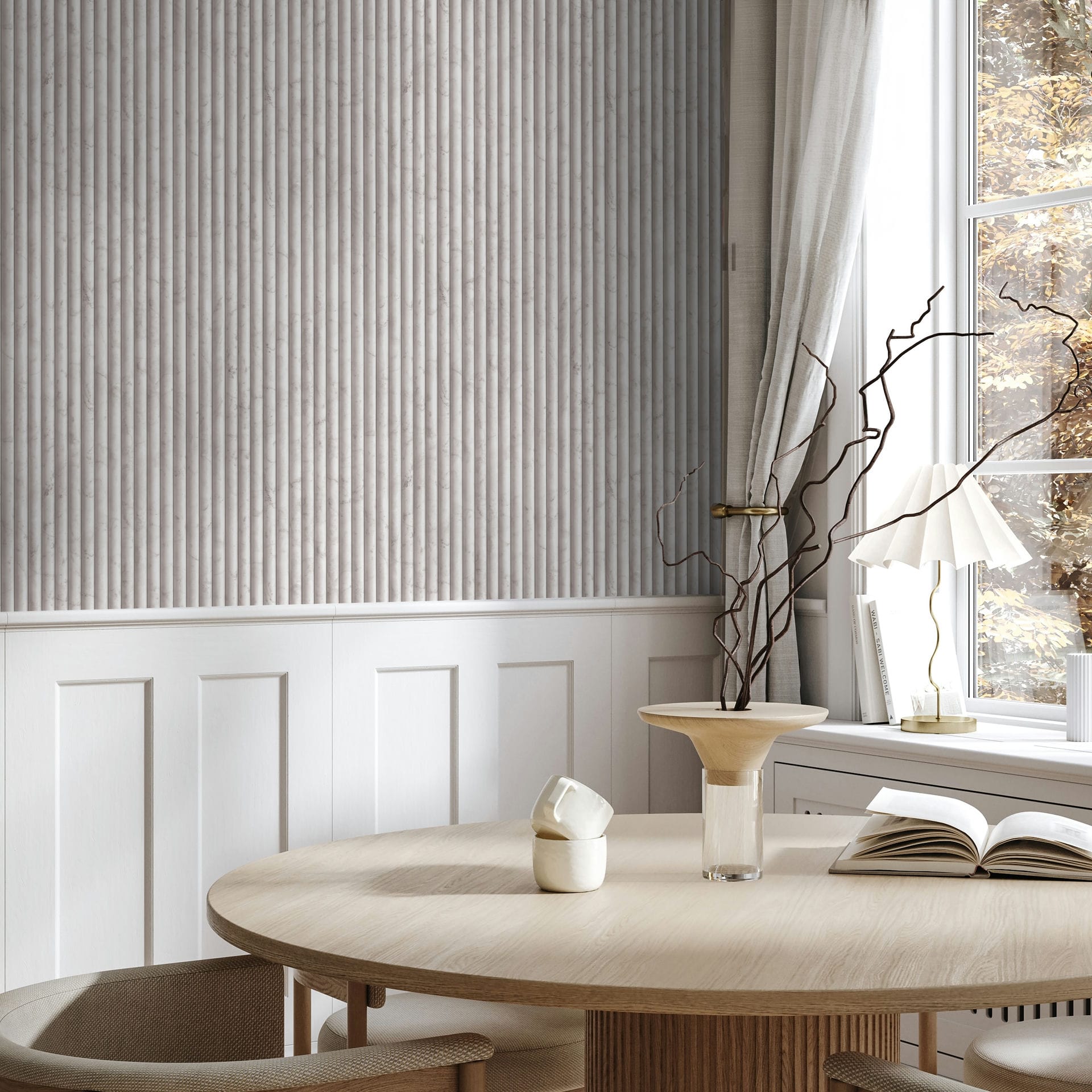 Marburg Mona 89004 Light beige-gray wallpaper with narrow vertical ribbed stripes above white wainscoting, shown in a dining area with a round table, chairs, a window with curtains, a table lamp, an open book, a cup, and a vase with branches.