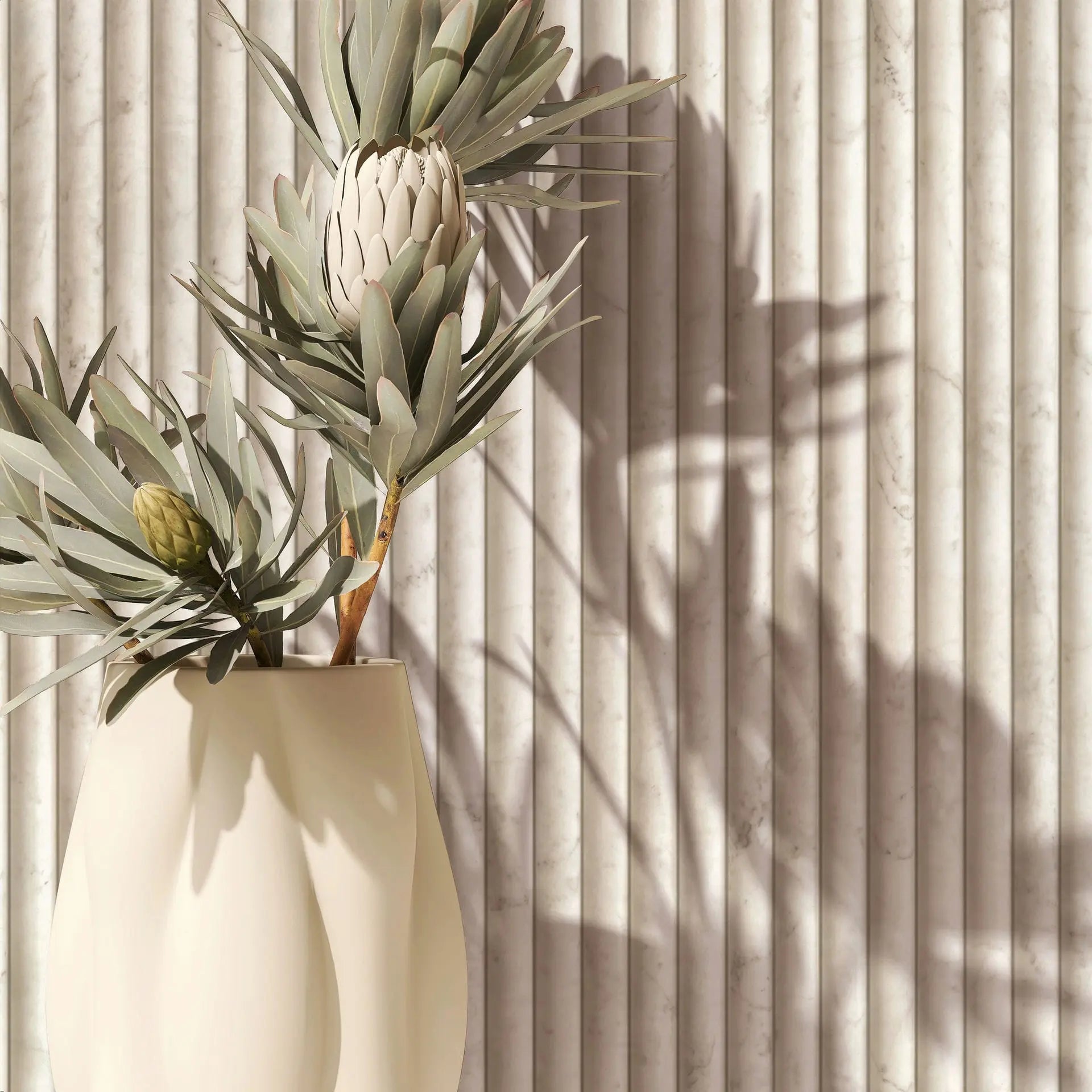 Marburg Mona 89006 Close-up of beige vertical fluted wallpaper with subtle marble veining, styled with a cream vase holding protea stems that cast soft shadows on the wall.