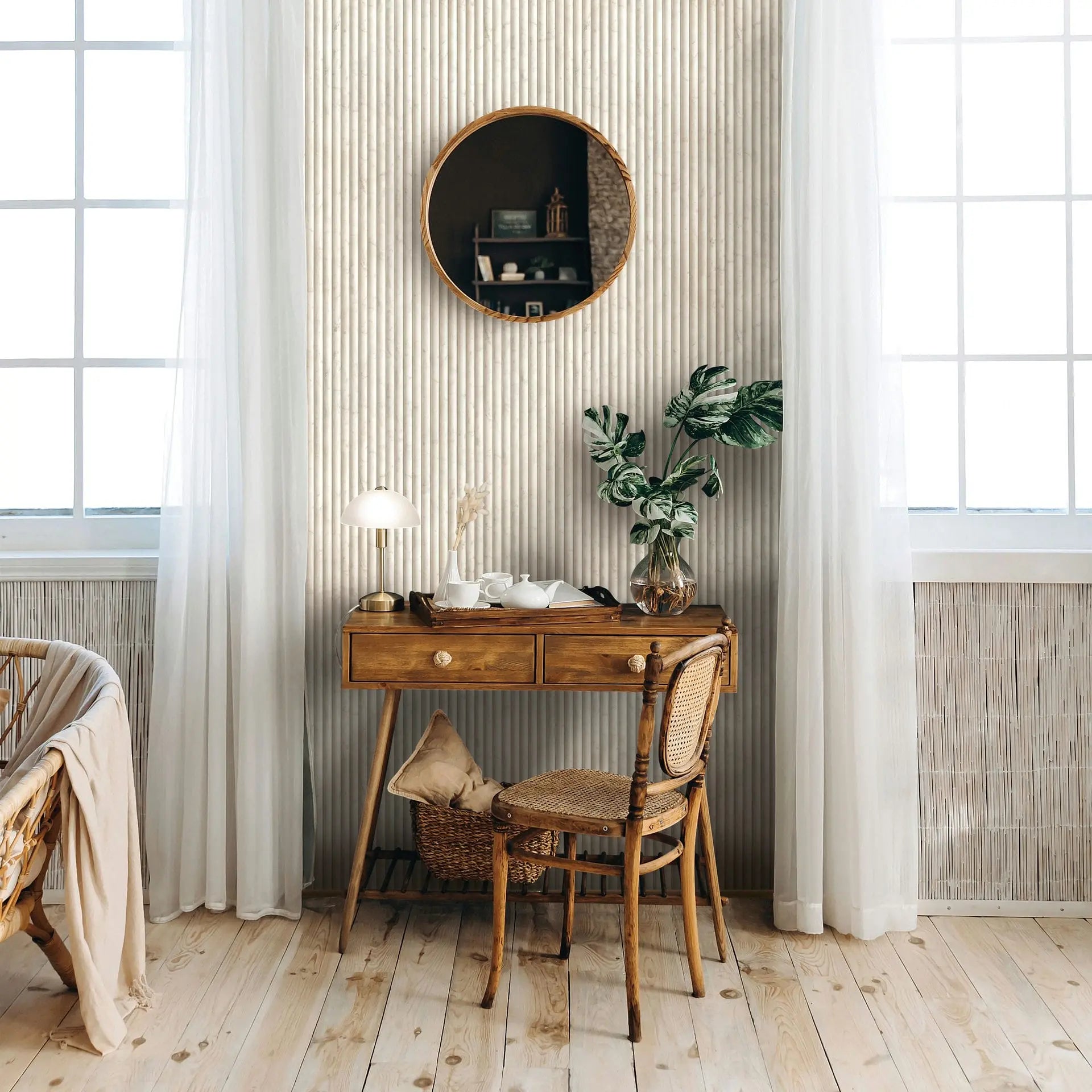 Marburg Mona 89006 Room scene featuring light beige vertical ribbed stripe wallpaper behind a wood desk and chair, with a round mirror, sheer curtains over large windows, a table lamp, a tray with a teapot and cups, and a leafy plant in a glass vase.