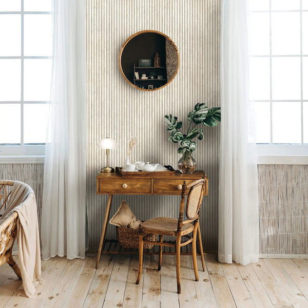 Marburg Mona 89006 Room scene featuring light beige vertical ribbed stripe wallpaper behind a wood desk and chair, with a round mirror, sheer curtains over large windows, a table lamp, a tray with a teapot and cups, and a leafy plant in a glass vase.