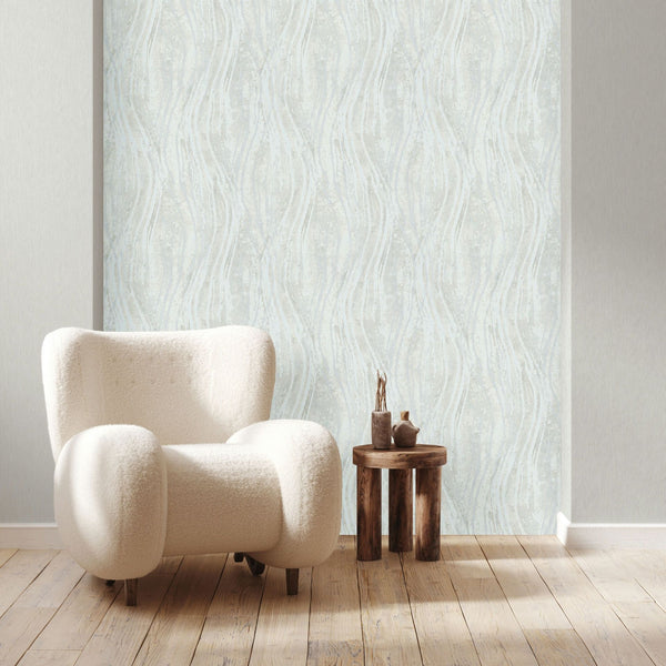 Marburg Naomi 82497 Living room scene featuring a gray and white wavy stripe wallpaper on a feature panel, a cream upholstered armchair, a small round wooden stool with decorative objects, and light wood flooring.