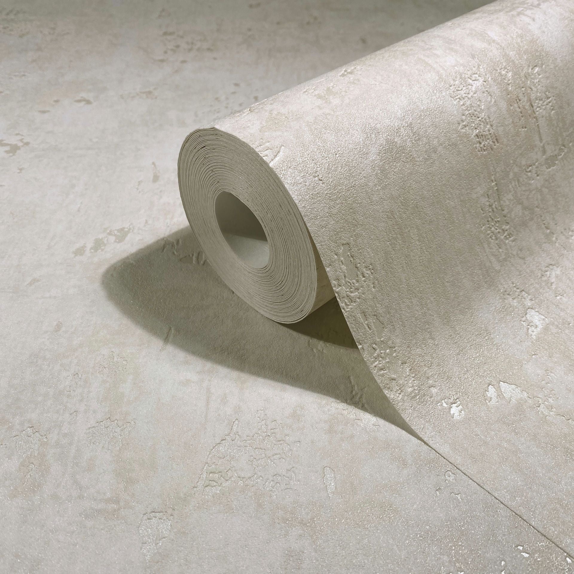 Marburg Naomi 82498 Close-up of a beige textured wallpaper roll with a subtle plaster-like pattern, partially unrolled on the same material.