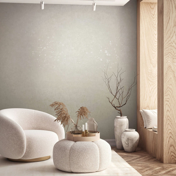 Marburg Naomi 82498 Neutral mottled wallpaper with a subtle sheen behind a rounded boucle armchair, a matching ottoman with a tray, tall ceramic vases with branches, and a built-in wooden bench.