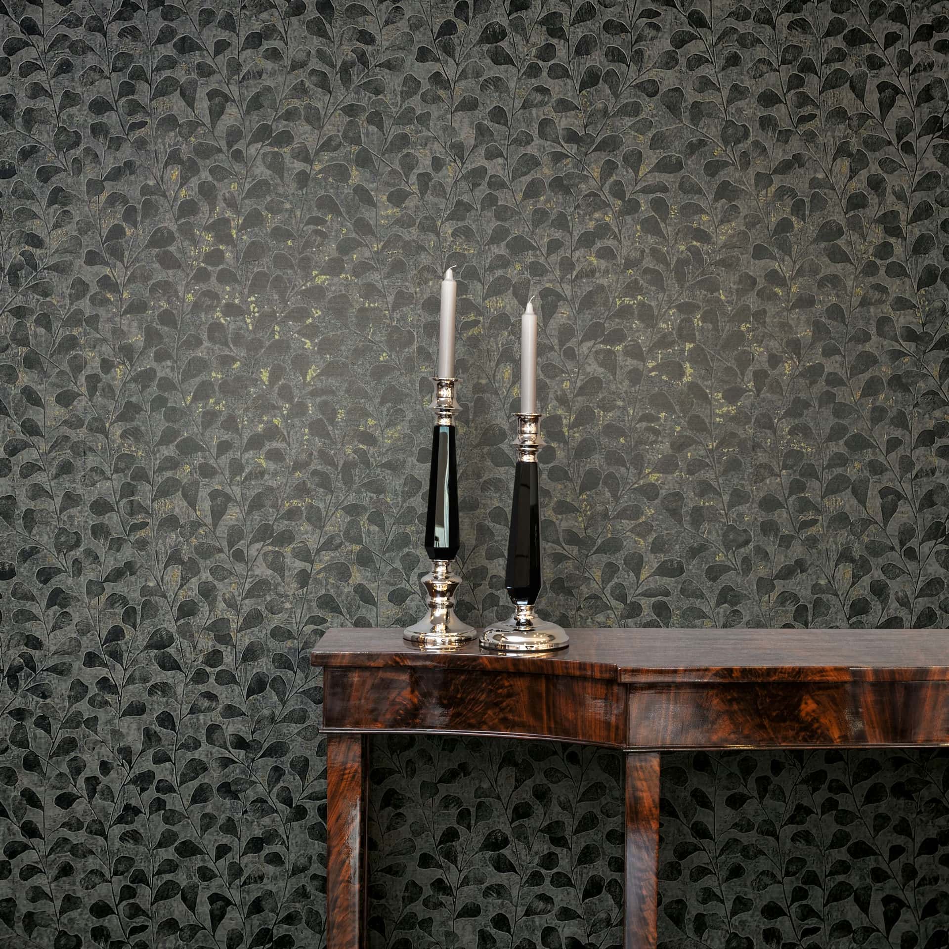 Marburg Naomi 82503 Dark gray leafy-pattern wallpaper behind a wood console table with two tall candlesticks and taper candles.