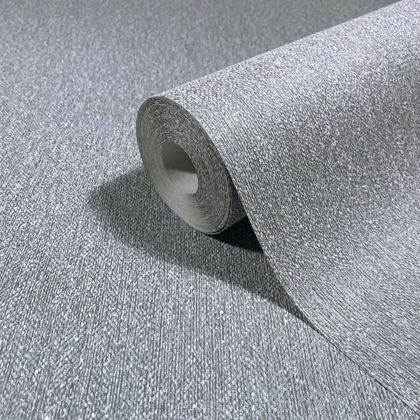 Marburg Naomi 82537 Close-up of a gray textured wallpaper roll, partly unrolled on a matching surface with fine vertical striations and speckled detail.