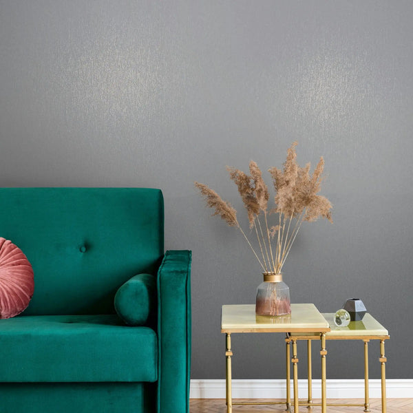 Marburg Naomi 82537 Gray textured wallpaper with a subtle sheen behind a teal sofa and brass nesting tables holding a ribbed glass vase with dried grasses and small decor.