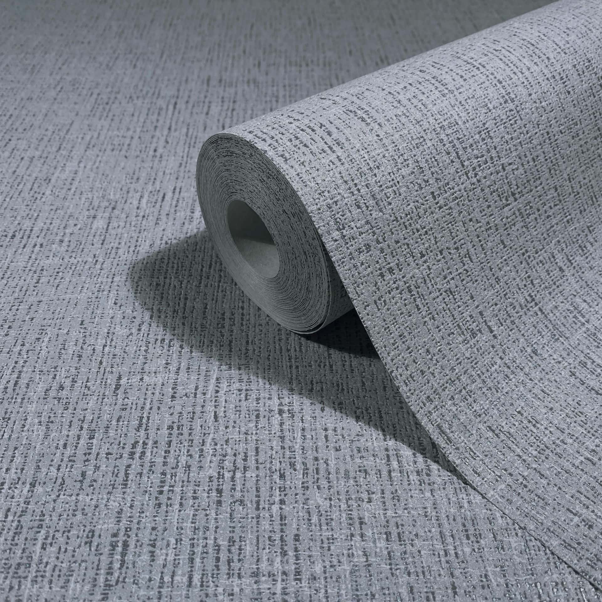 Marburg Naomi 82543 A gray wallpaper roll with a subtle crosshatch texture, partially unrolled on a matching surface.