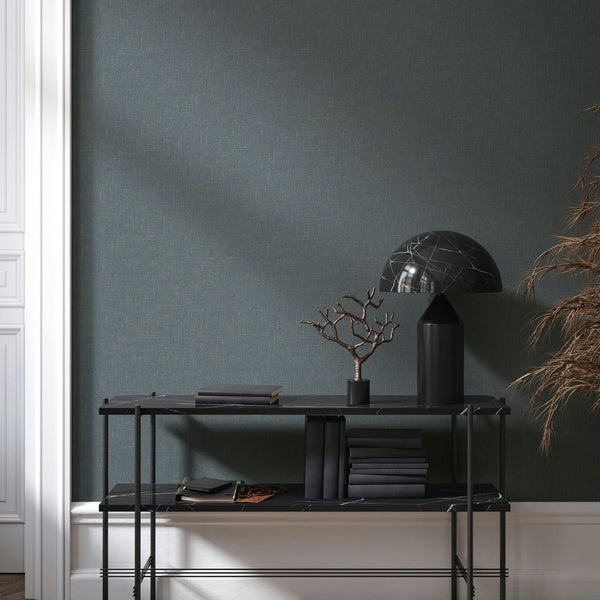 Marburg Naomi 82544 Dark crosshatch-textured wallpaper behind a slim black console table with a dome table lamp, stacked books, a small branch sculpture, dried grasses, and white wall moulding at the side.