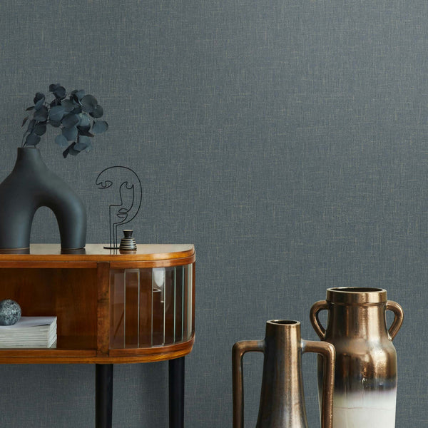 Marburg Naomi 82544 Dark gray crosshatch-effect wallpaper behind a curved wooden sideboard with a sculptural black vase with foliage, a wire ornament, and two tall metallic vases.