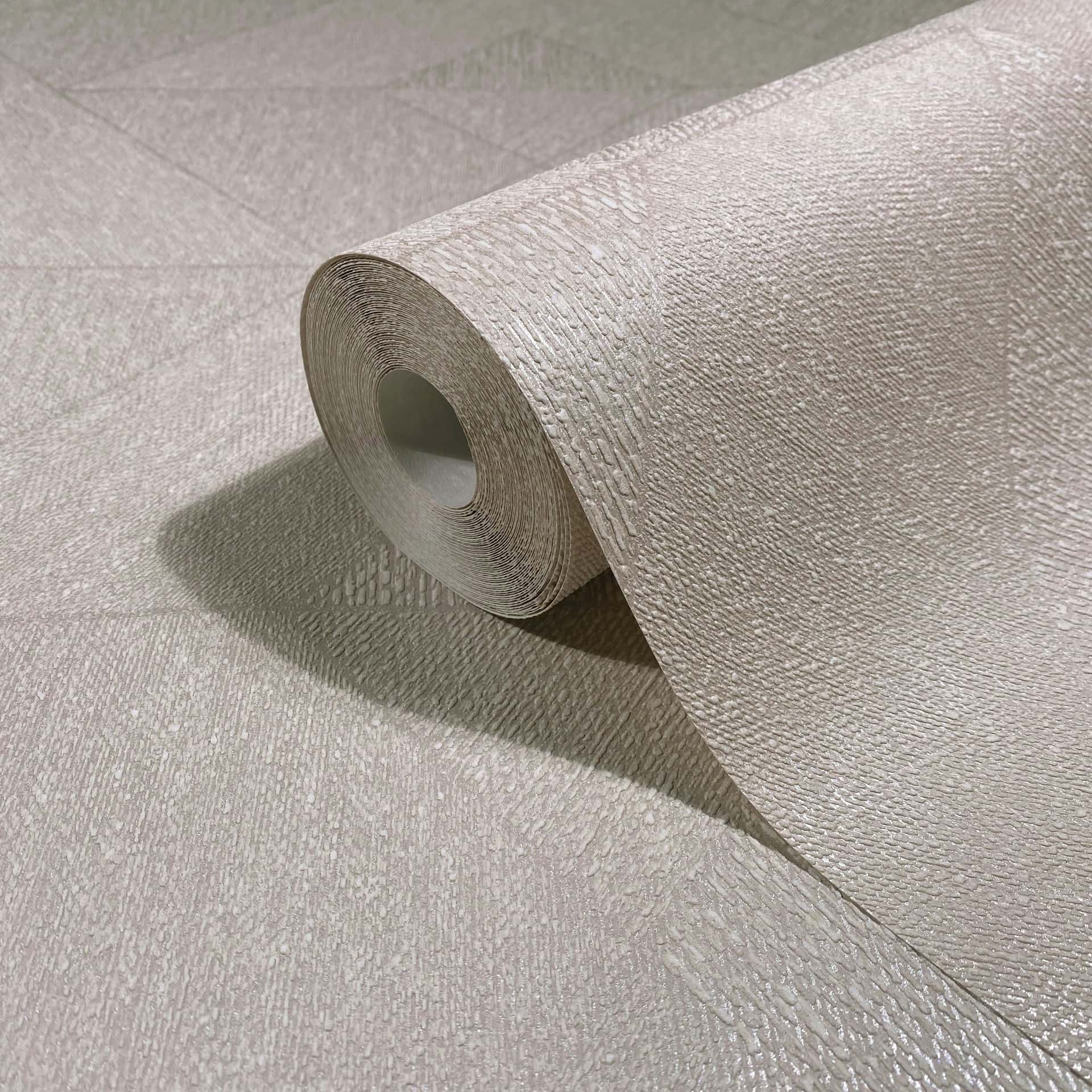 Marburg Naomi 82546 Close-up of a beige textured wallpaper roll resting on matching unrolled wallpaper, showing an embossed pattern of diagonal lines and small raised texture.