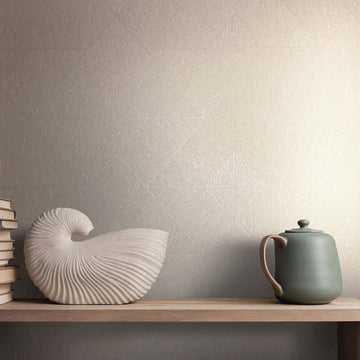 Marburg Naomi 82546 Beige wallpaper with a subtle textured geometric pattern behind a shelf styled with a shell-shaped sculpture, a stack of books, and a teapot.