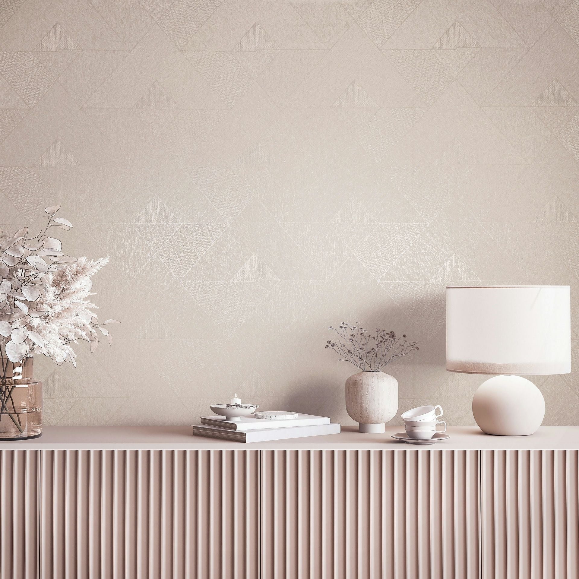 Marburg Naomi 82546 Beige wallpaper with a subtle geometric triangle pattern behind a fluted console styled with a table lamp, vases with dried stems, stacked books, and teacups.