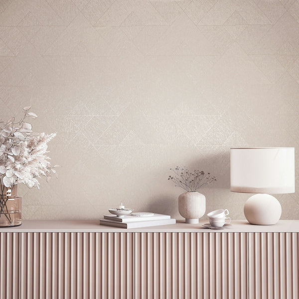 Marburg Naomi 82546 Beige wallpaper with a subtle geometric triangle pattern behind a fluted console styled with a table lamp, vases with dried stems, stacked books, and teacups.