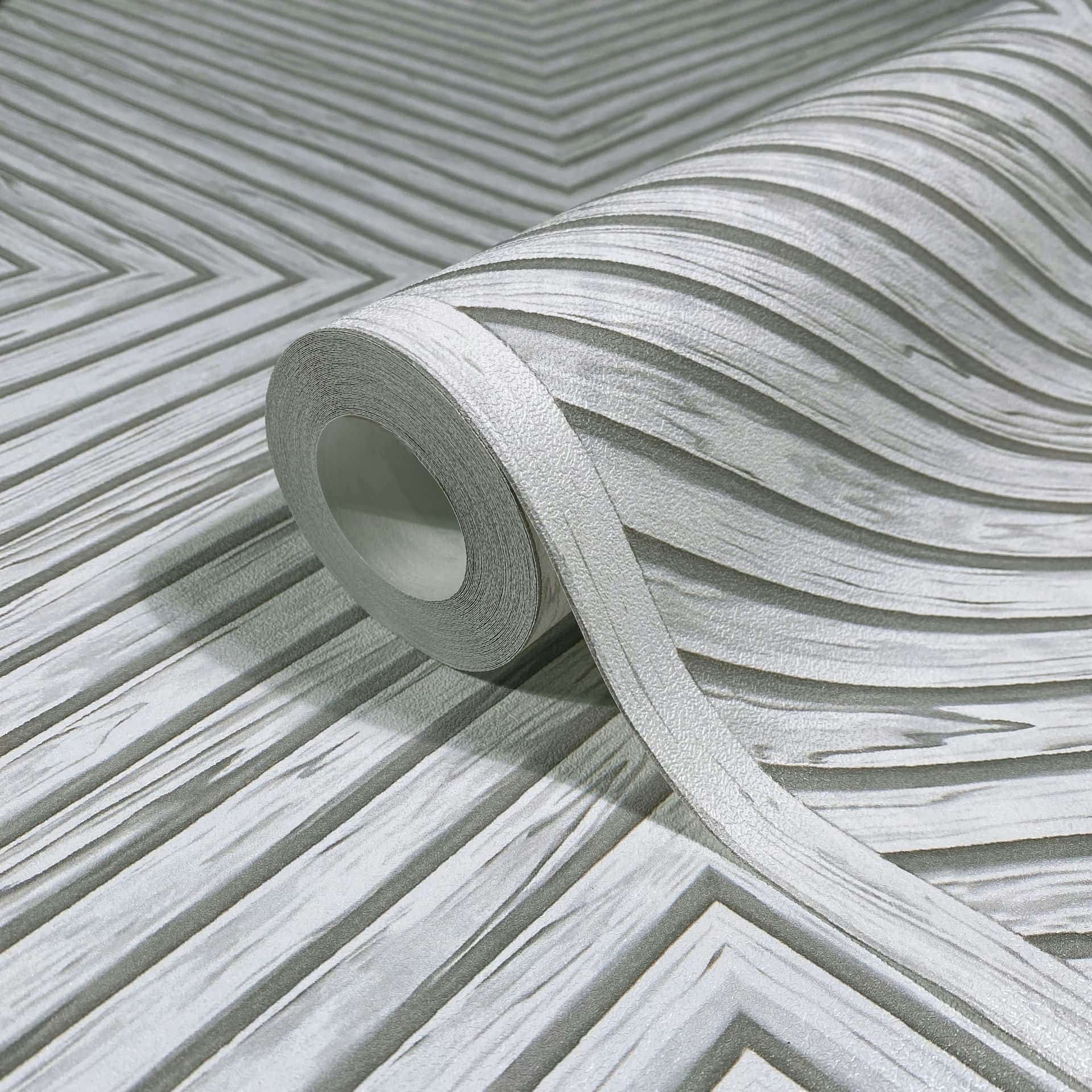 Marburg Naomi 89021 Close-up product view of a wallpaper roll partially unrolled across a gray and white chevron pattern with textured, layered stripes.