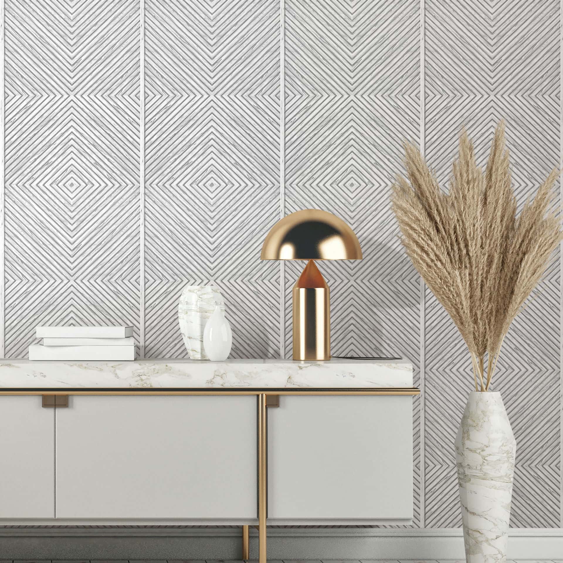 Marburg Naomi 89021 Gray and white wallpaper with a concentric diamond line pattern behind a console with a marble-look top, a brass dome lamp, two vases, stacked books, and a tall vase of pampas grass.